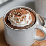 Keto Chocolate Mug Cake in a mug with cream and chocolate powder on it