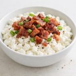 A savory bowl of cottage cheese topped with crispy bacon crumbs, combining a creamy base with a crisp, salty finish.