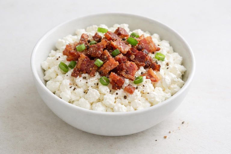 A savory bowl of cottage cheese topped with crispy bacon crumbs, combining a creamy base with a crisp, salty finish.